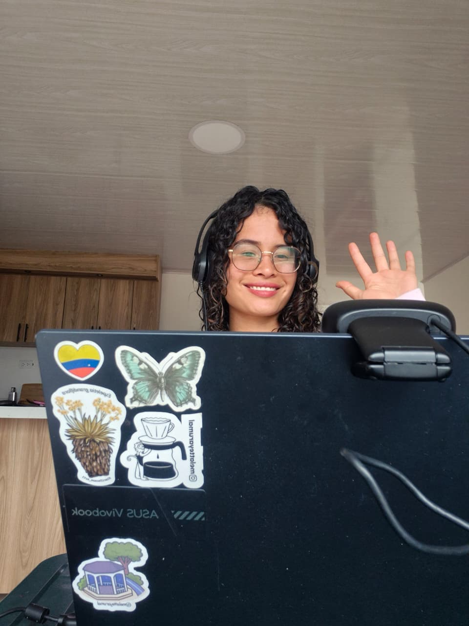 Profesora de español saludando durante una clase en línea desde casa, frente a su portátil
